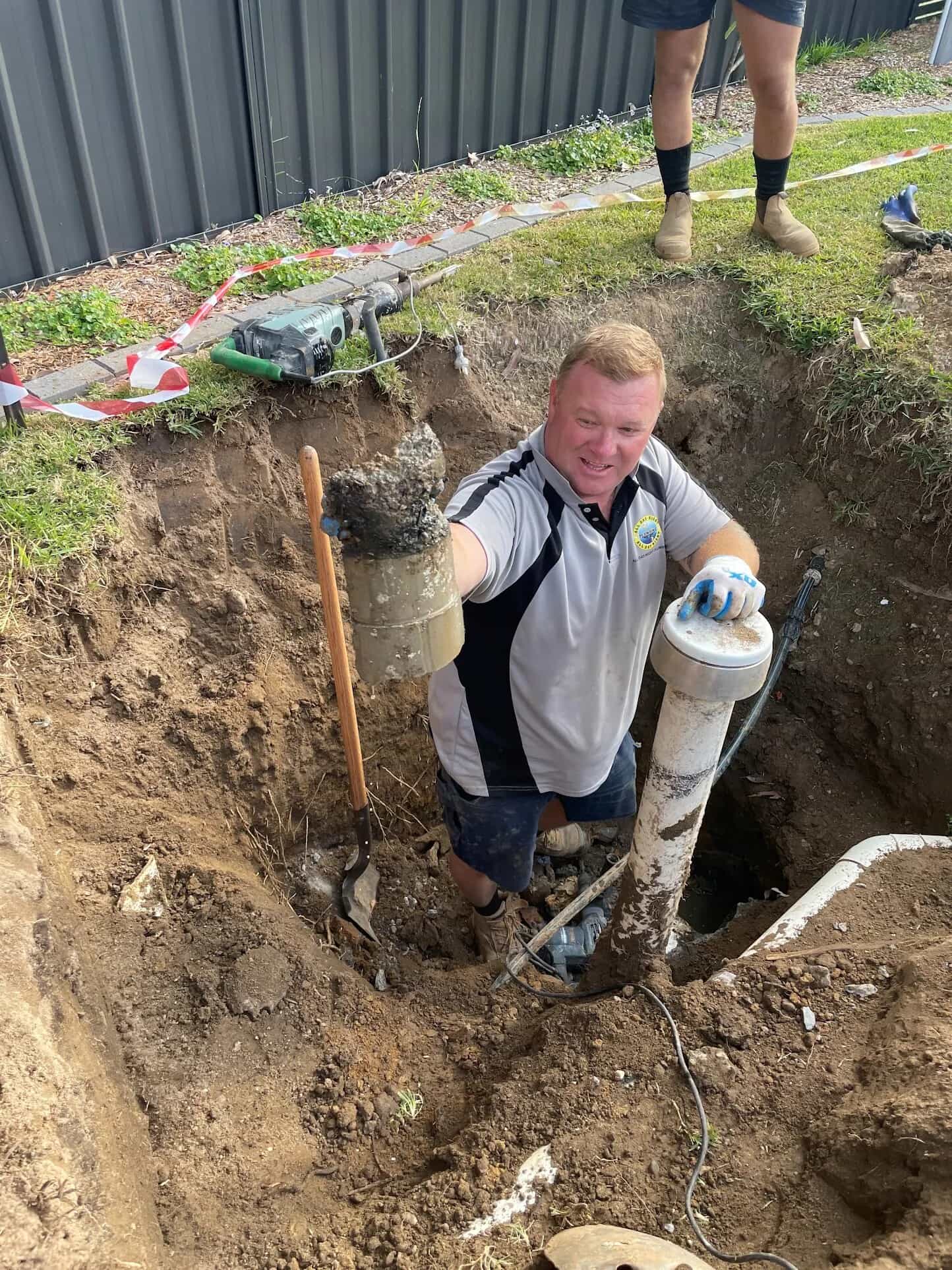 Scott Johnstone holding a concrete-obstructed sewer fitting in an excavated trench