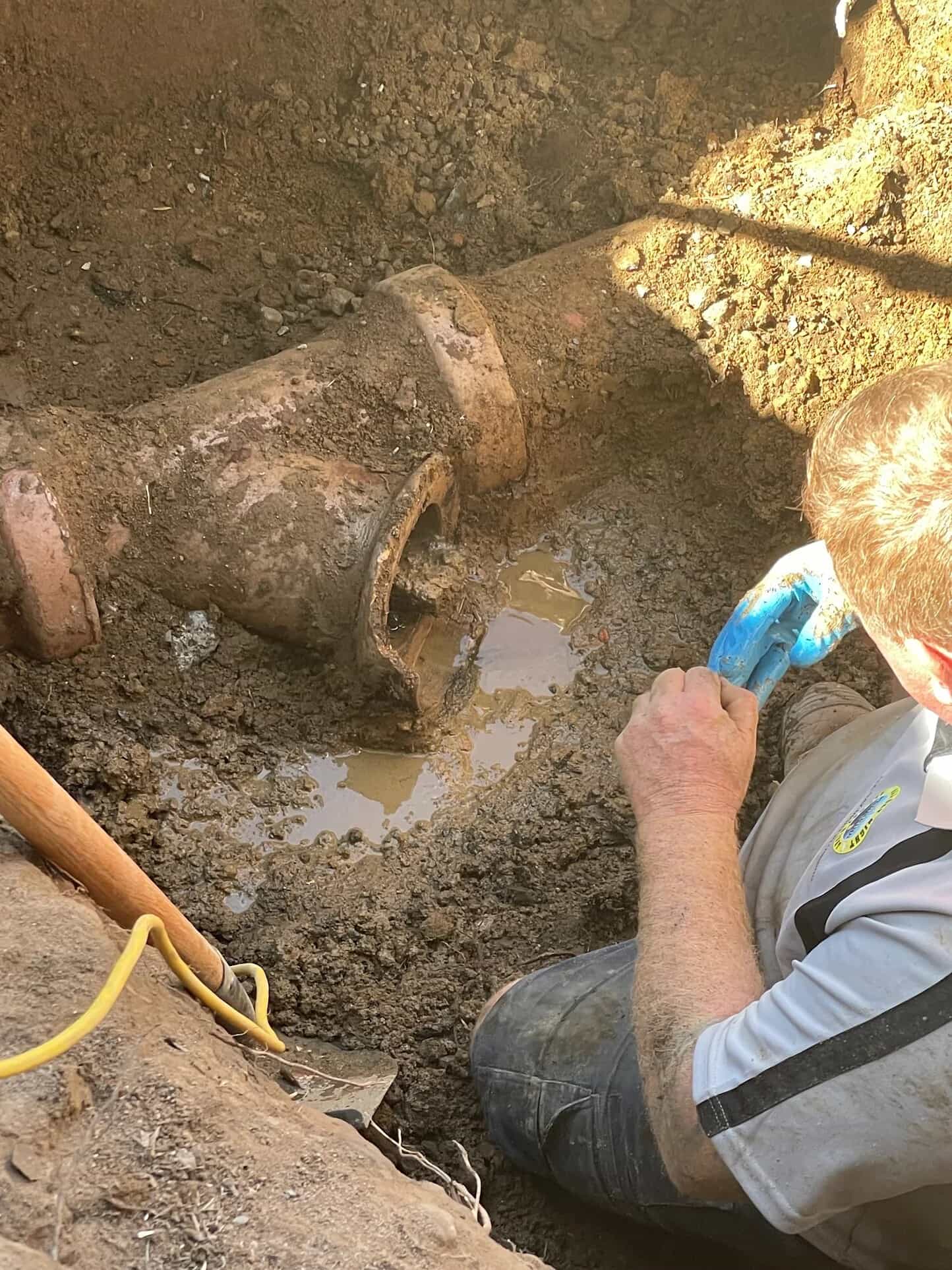 Concrete-obstructed sewer pipework exposed inside a yard trench