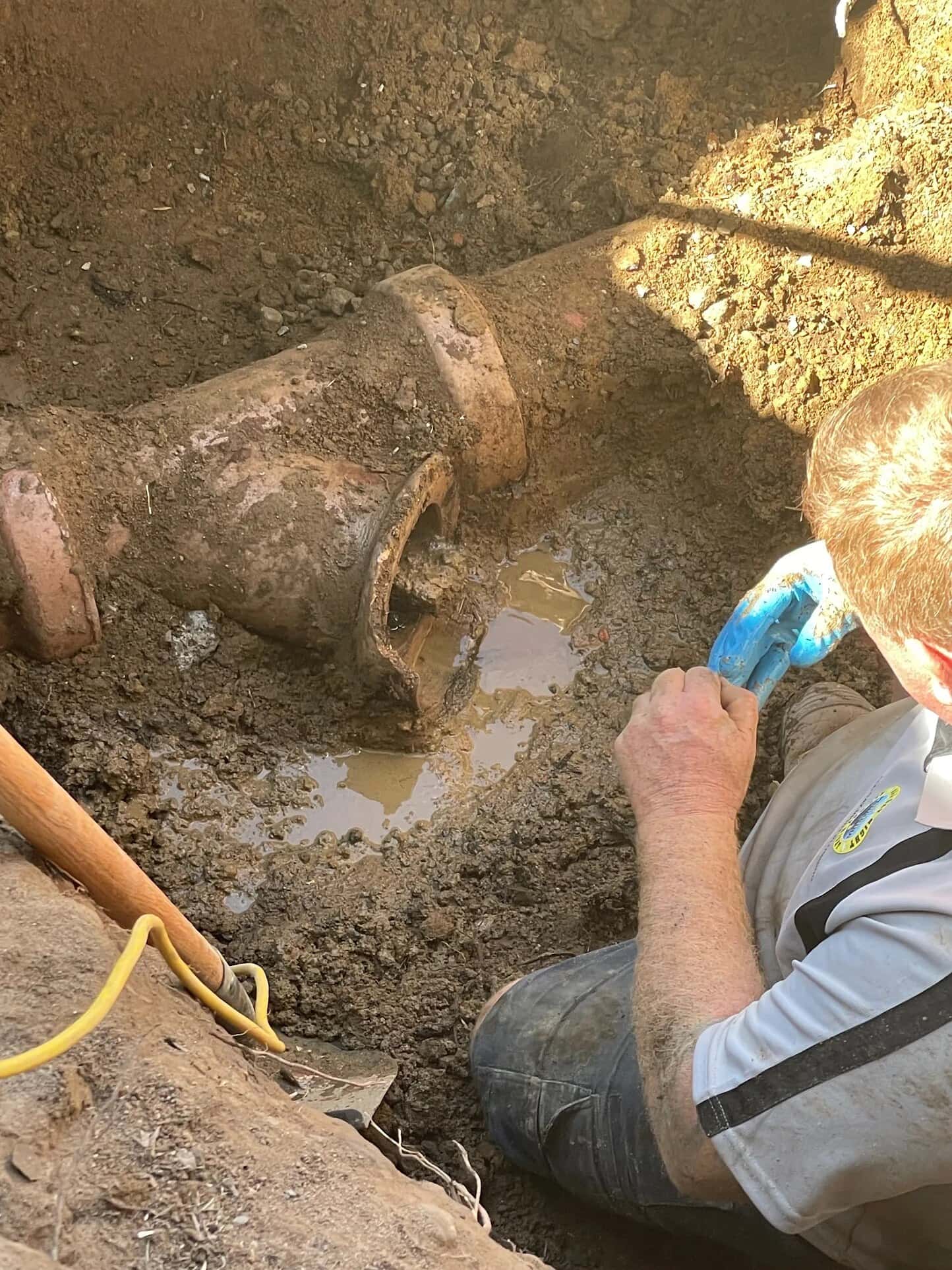Concrete-obstructed sewer pipework exposed inside a yard trench