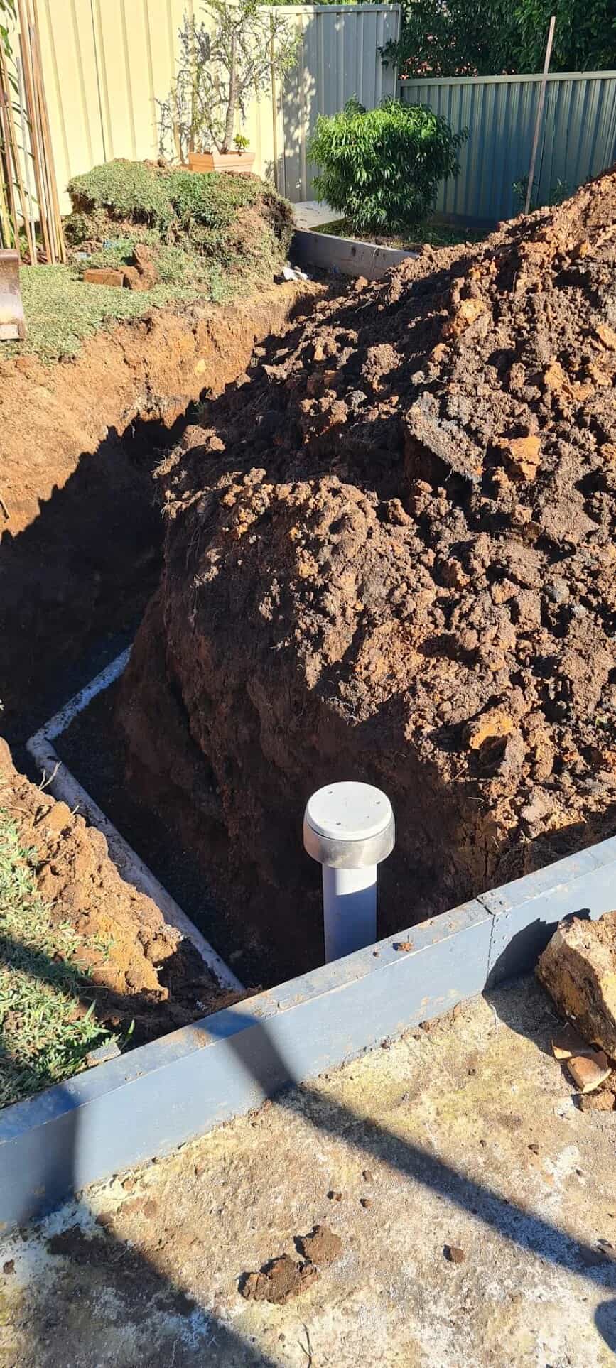 New PVC sewer pipe and capped inspection riser in a deep yard trench