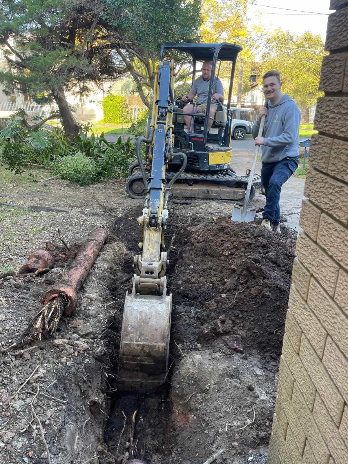 Excavator working beside a root-damaged drain pipe