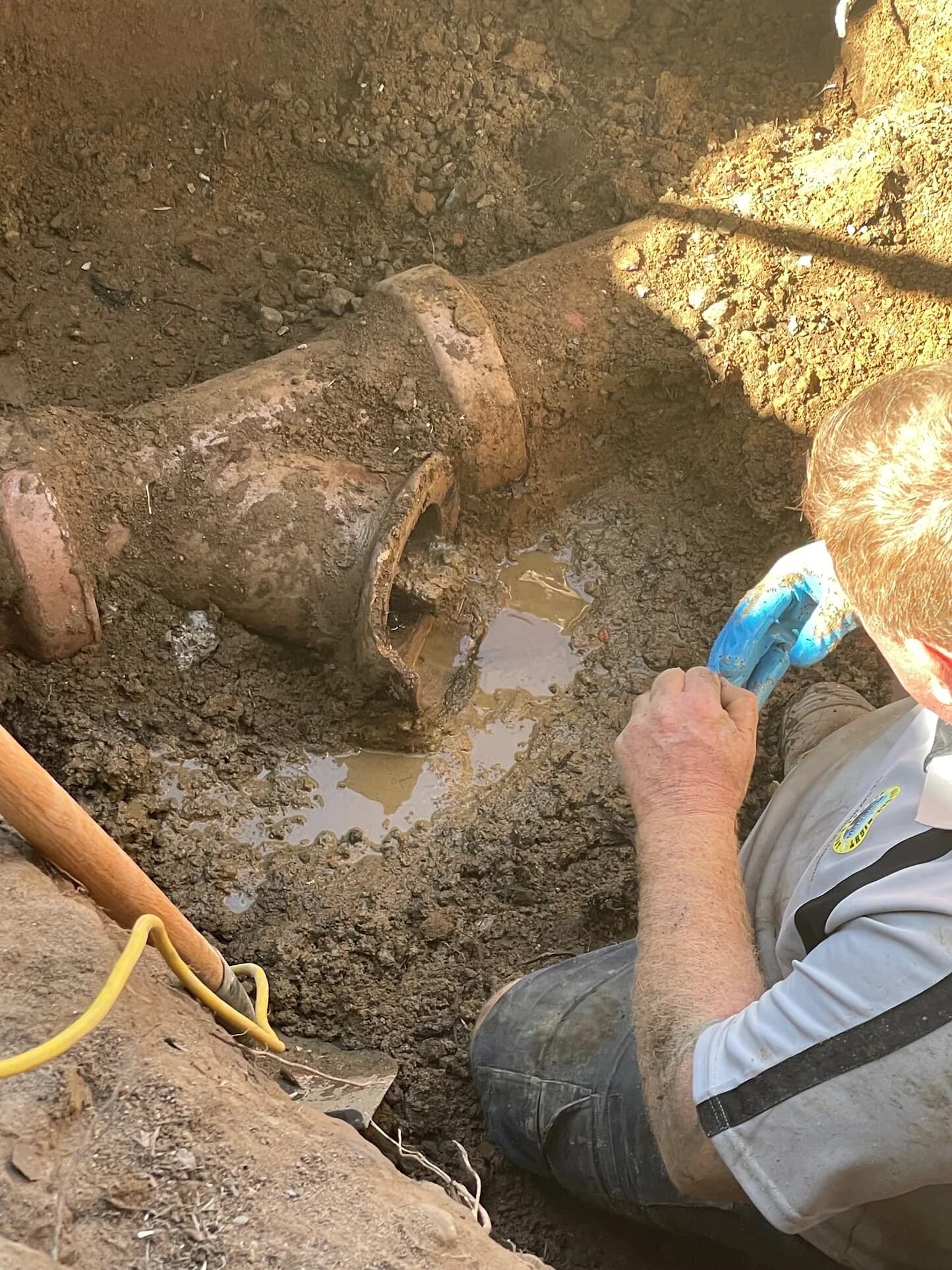 Concrete-obstructed sewer pipework exposed inside a yard trench