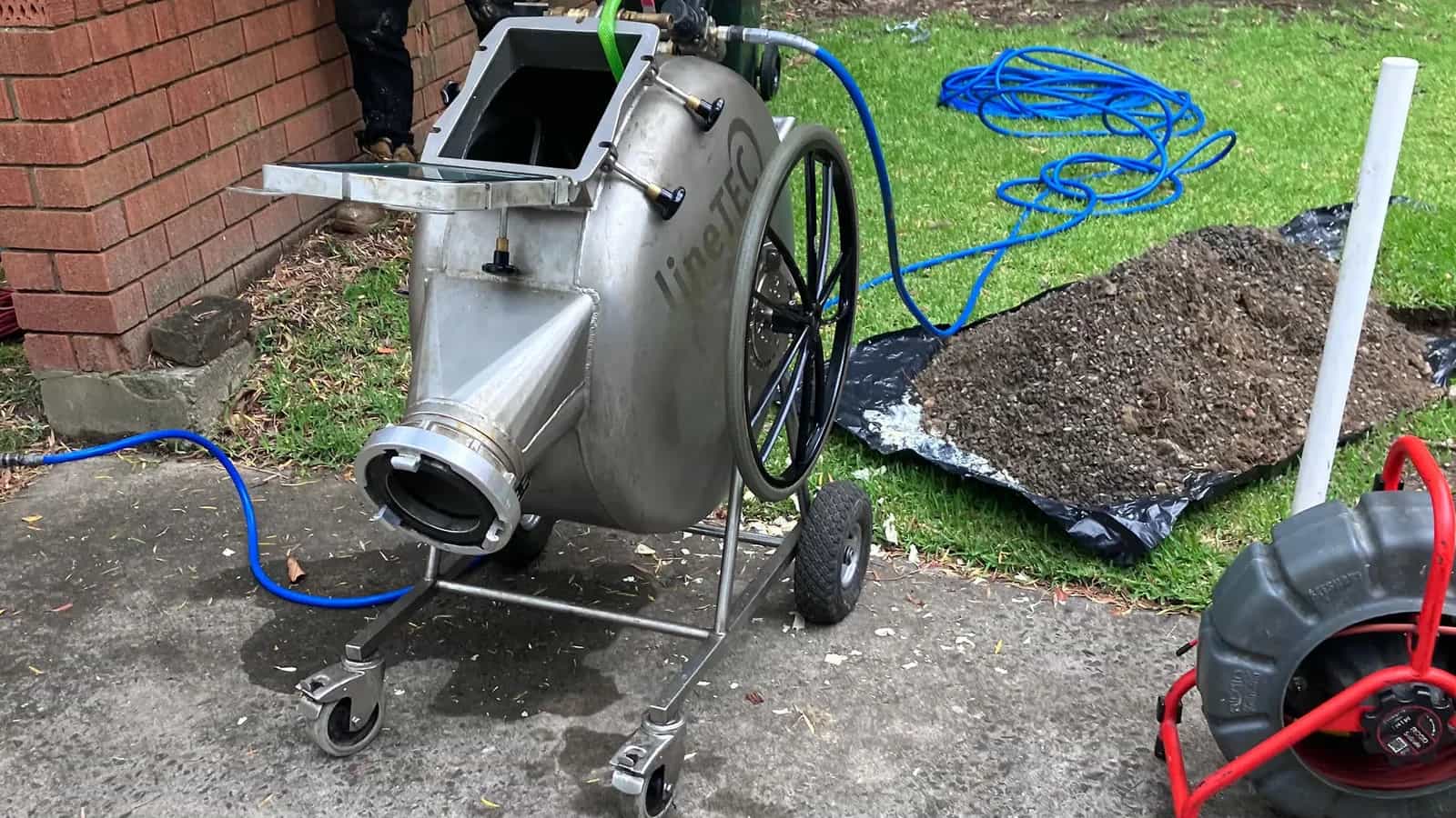 Stainless steel pipe relining drum beside an excavated outdoor drain line
