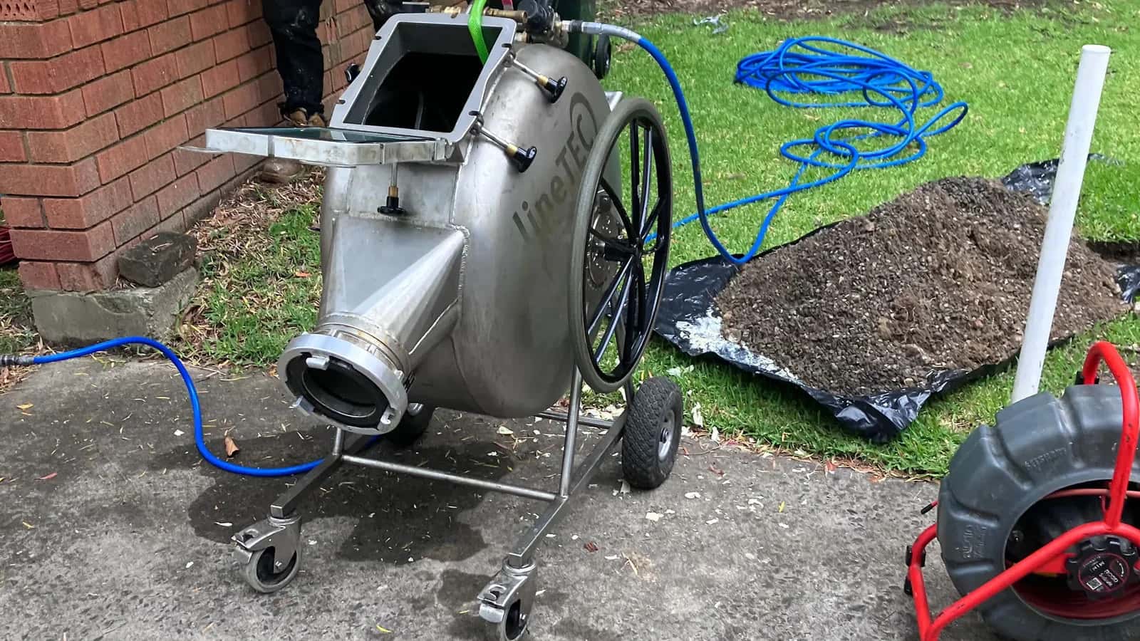 Stainless steel pipe relining drum beside an excavated outdoor drain line