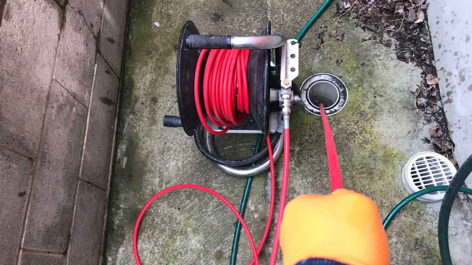 Red drain jetting hose reel feeding into an outdoor drain access